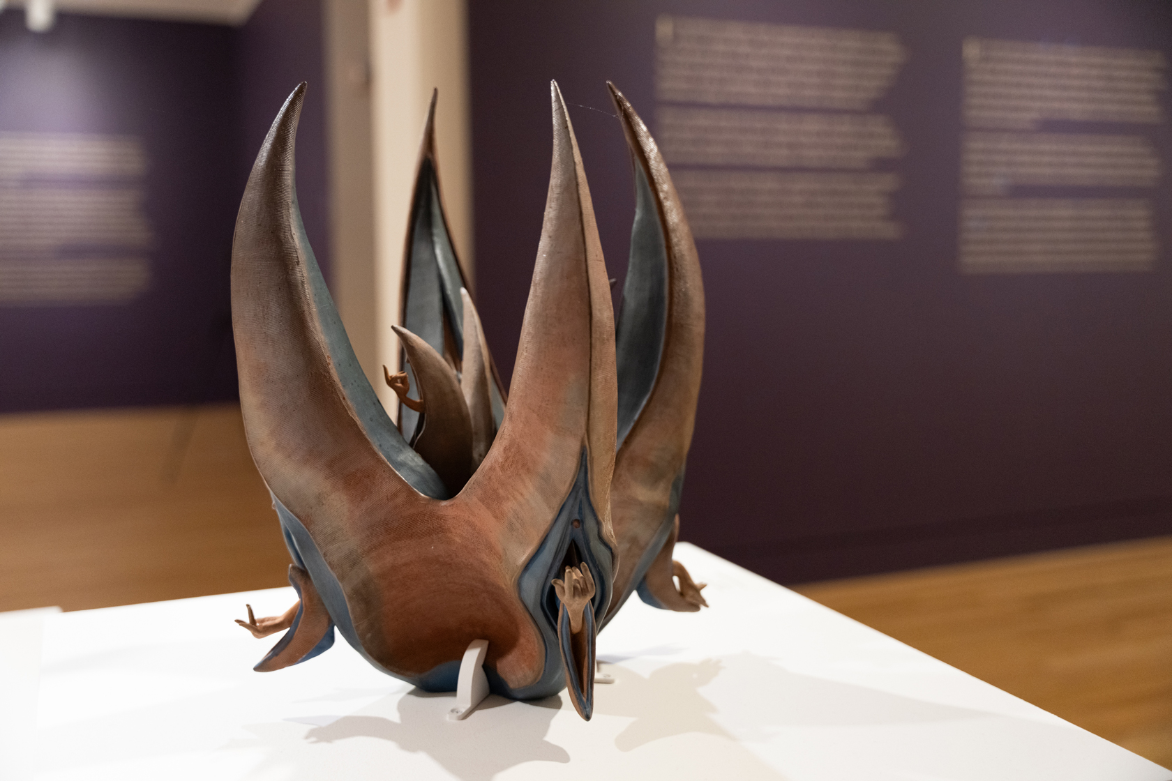 Close-up of a ceramic vessel with four large pointy spikes and hands emerging from vulvas on its sides