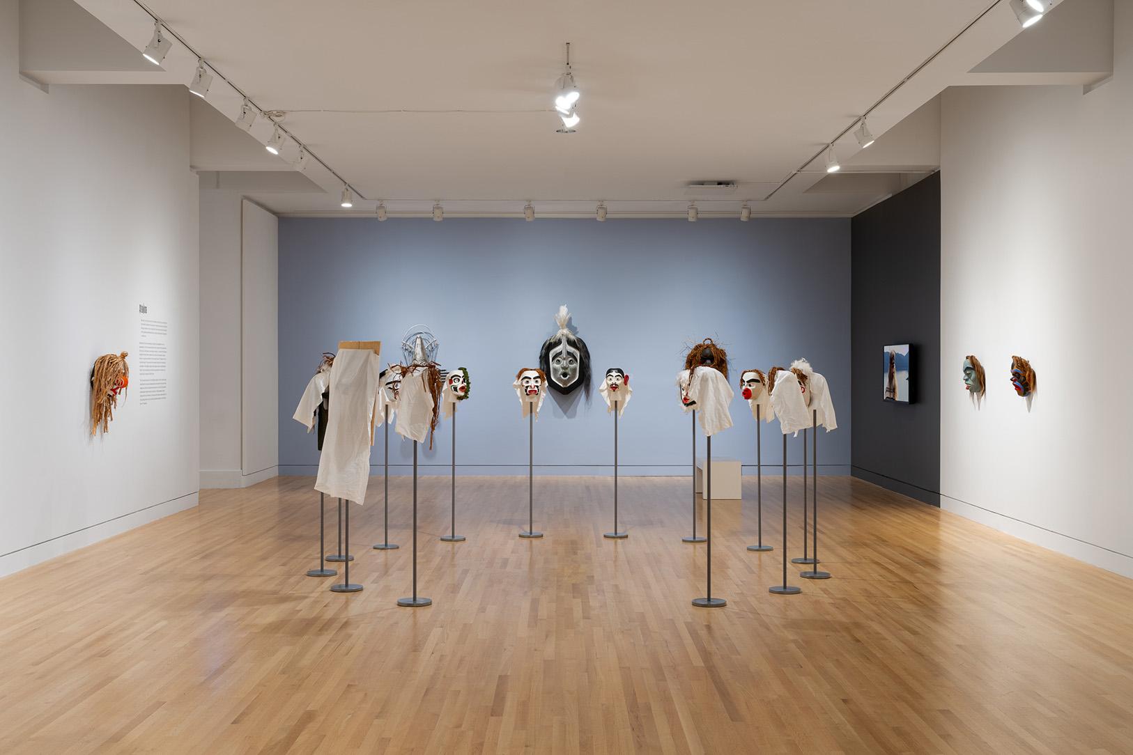 A set of masks arranged on stands in a circle in a large room. Other masks are mounted on the surround walls
