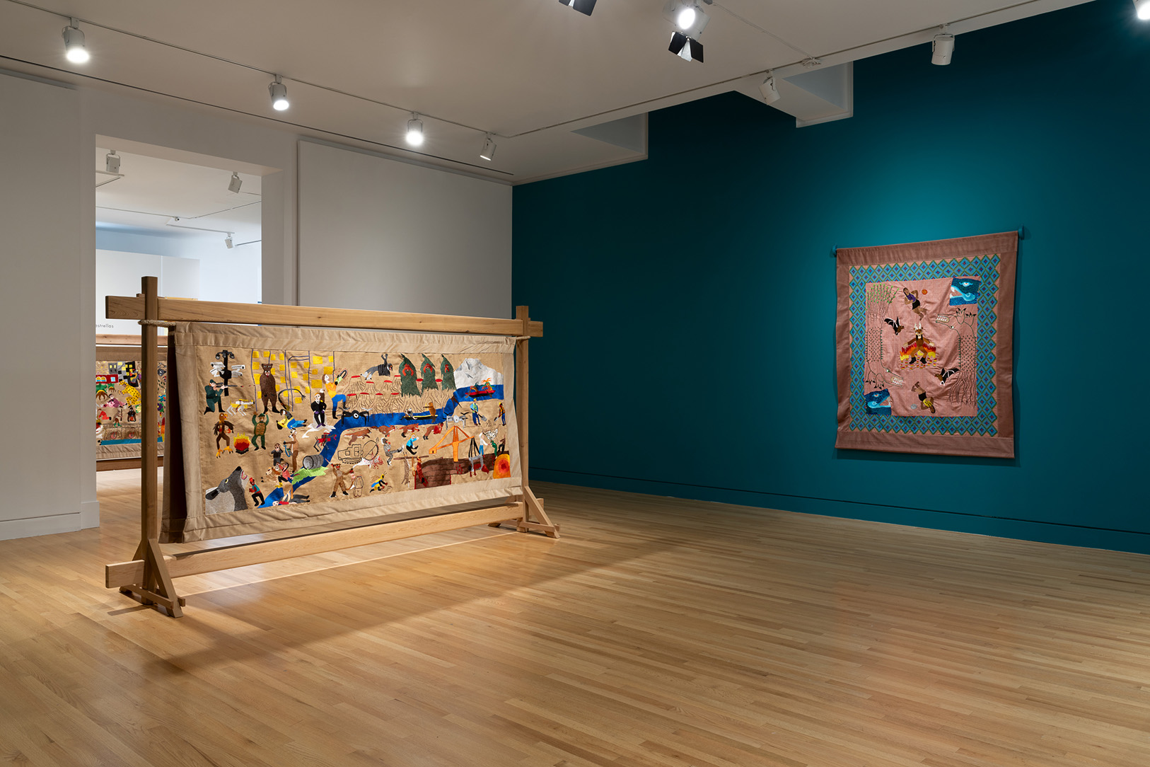 A pair of large fabric artworks in a gallery space, one in a freestanding fixture and the other hanging on a wall