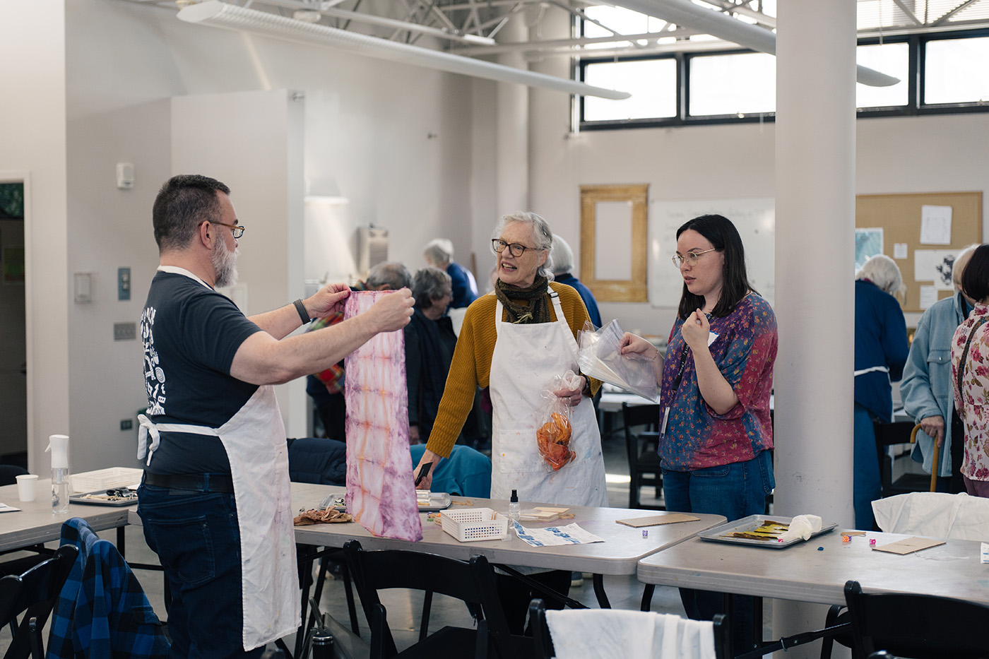 A person holds up a freshly dyed handkerchief for a pair of people on the other side of a table