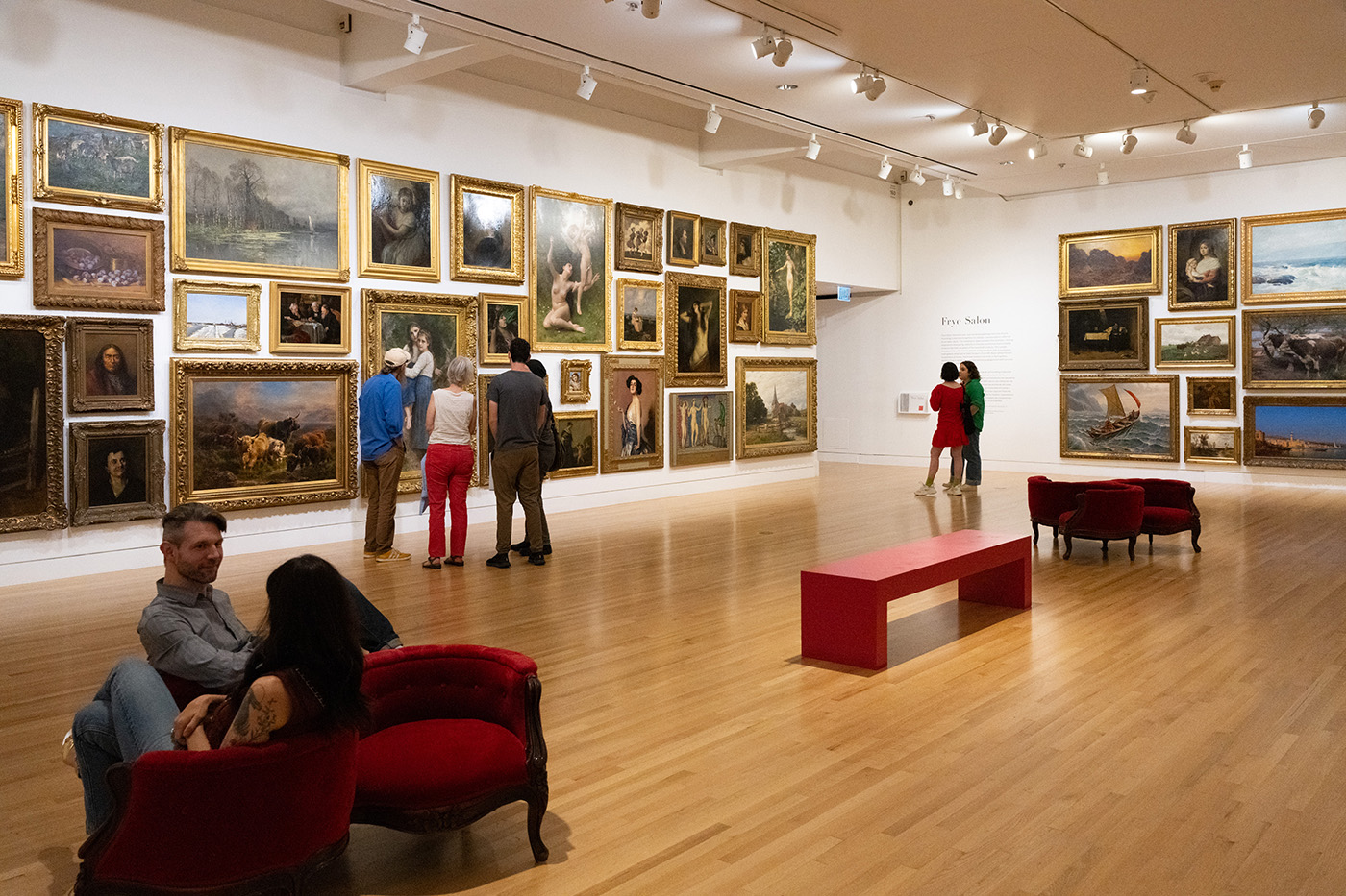 People in a large gallery space with a large number of oil paintings on the walls