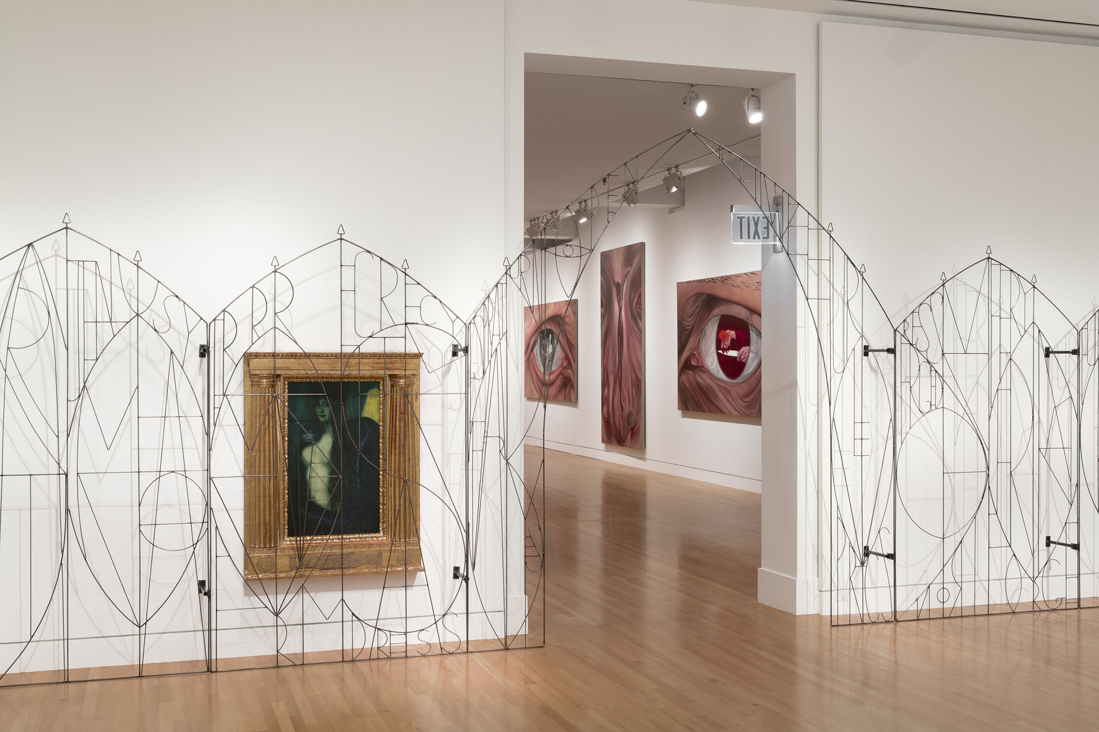 Museum gallery with three artworks, a metal gate, and white walls