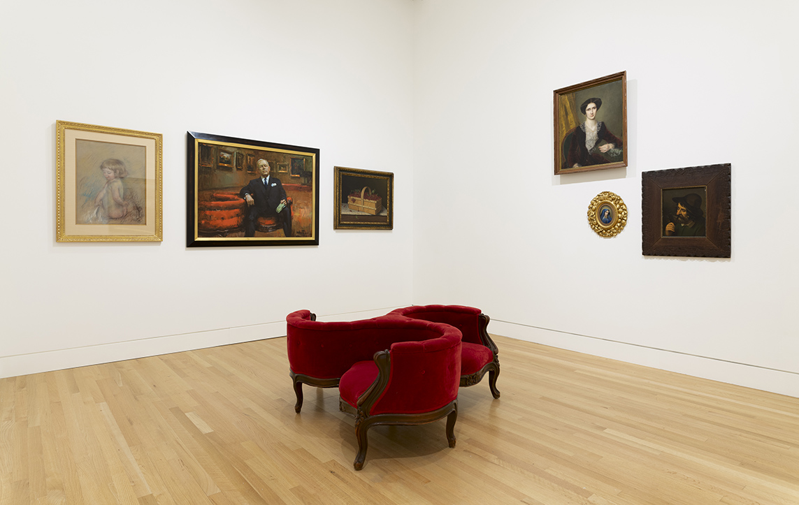 Six artworks hanging on a white gallery wall with a red gossip chair in the middle of the floor