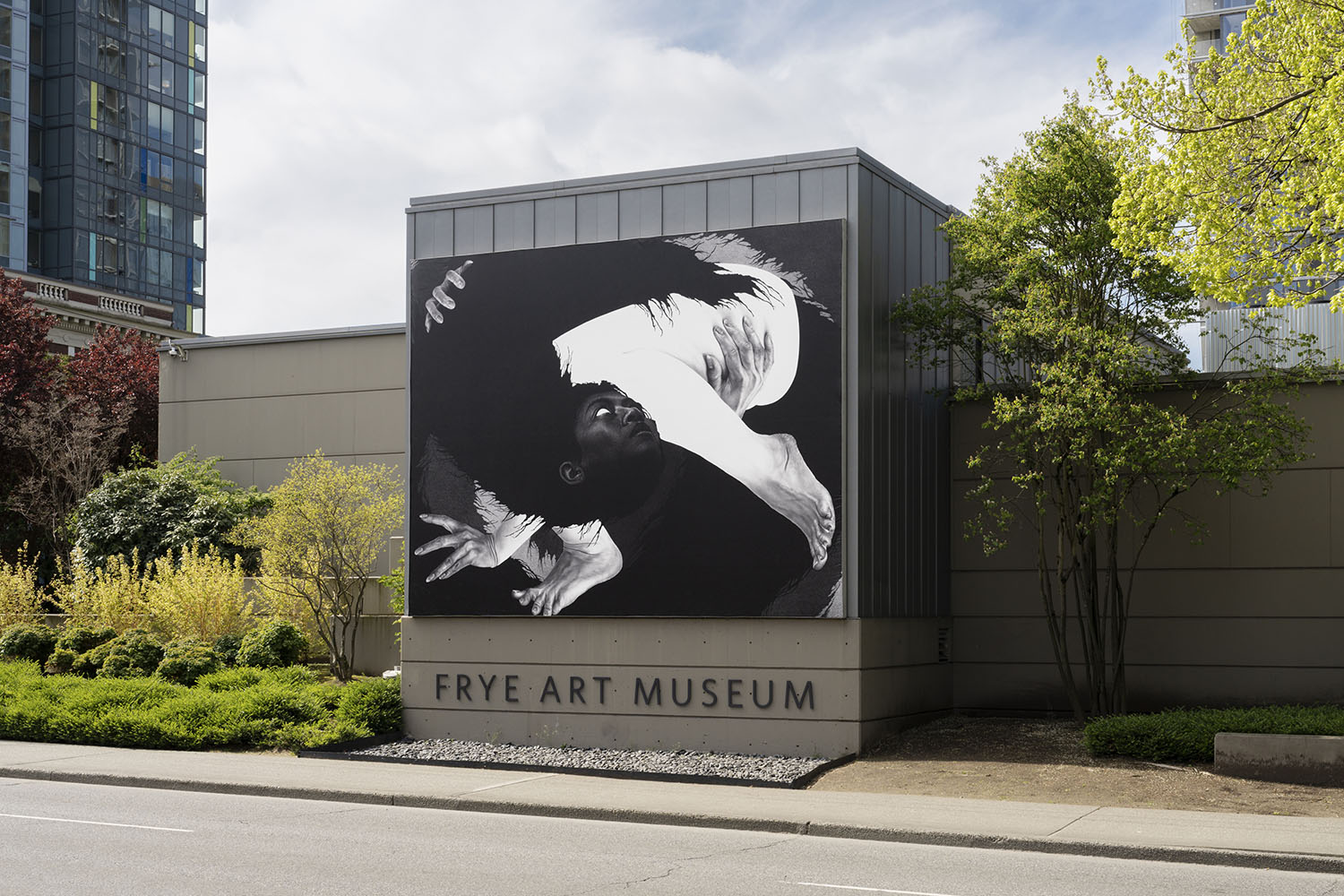 Photo of a large black and white figurative banner installed on a grey building next to the road