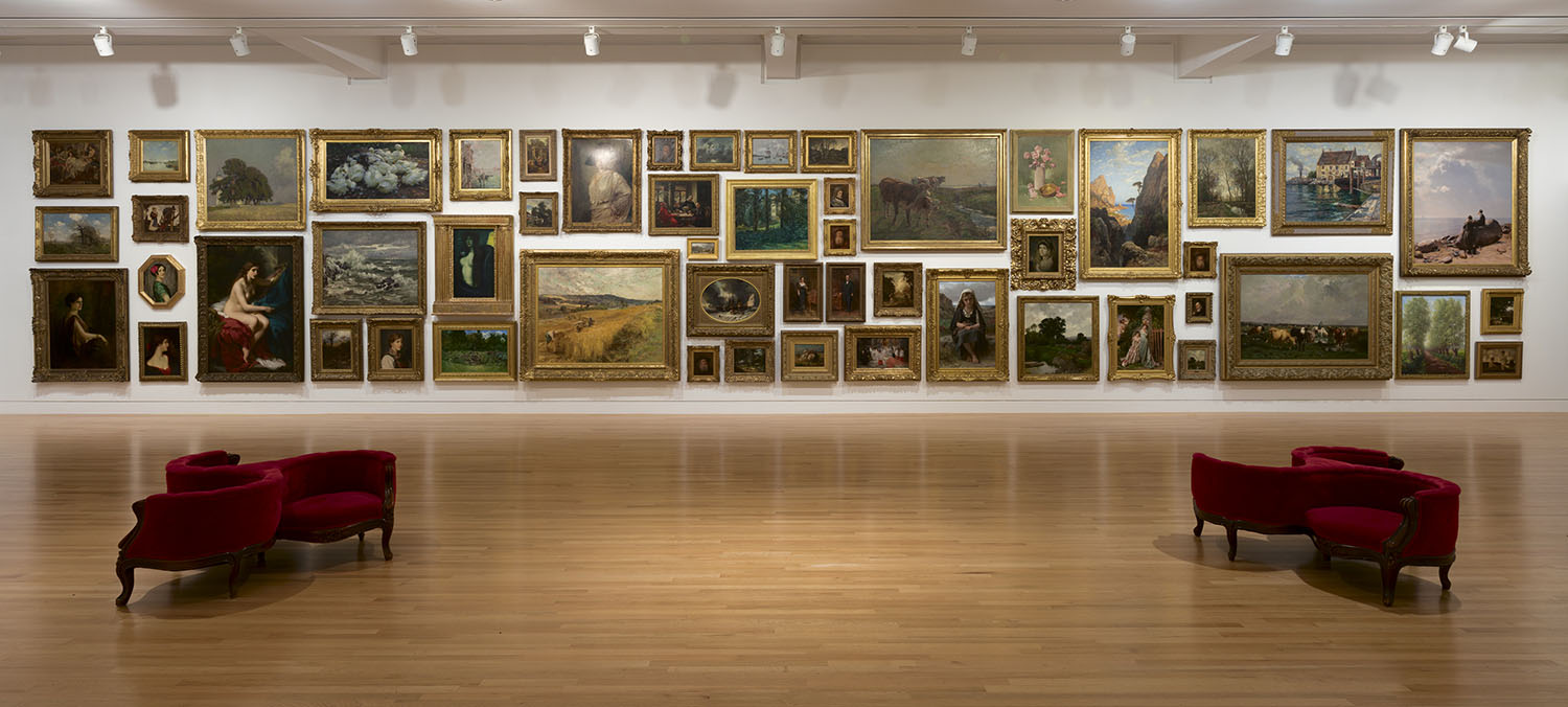 Paintings hung floor to ceiling in a gallery with white walls, two red gossip chairs on the floor