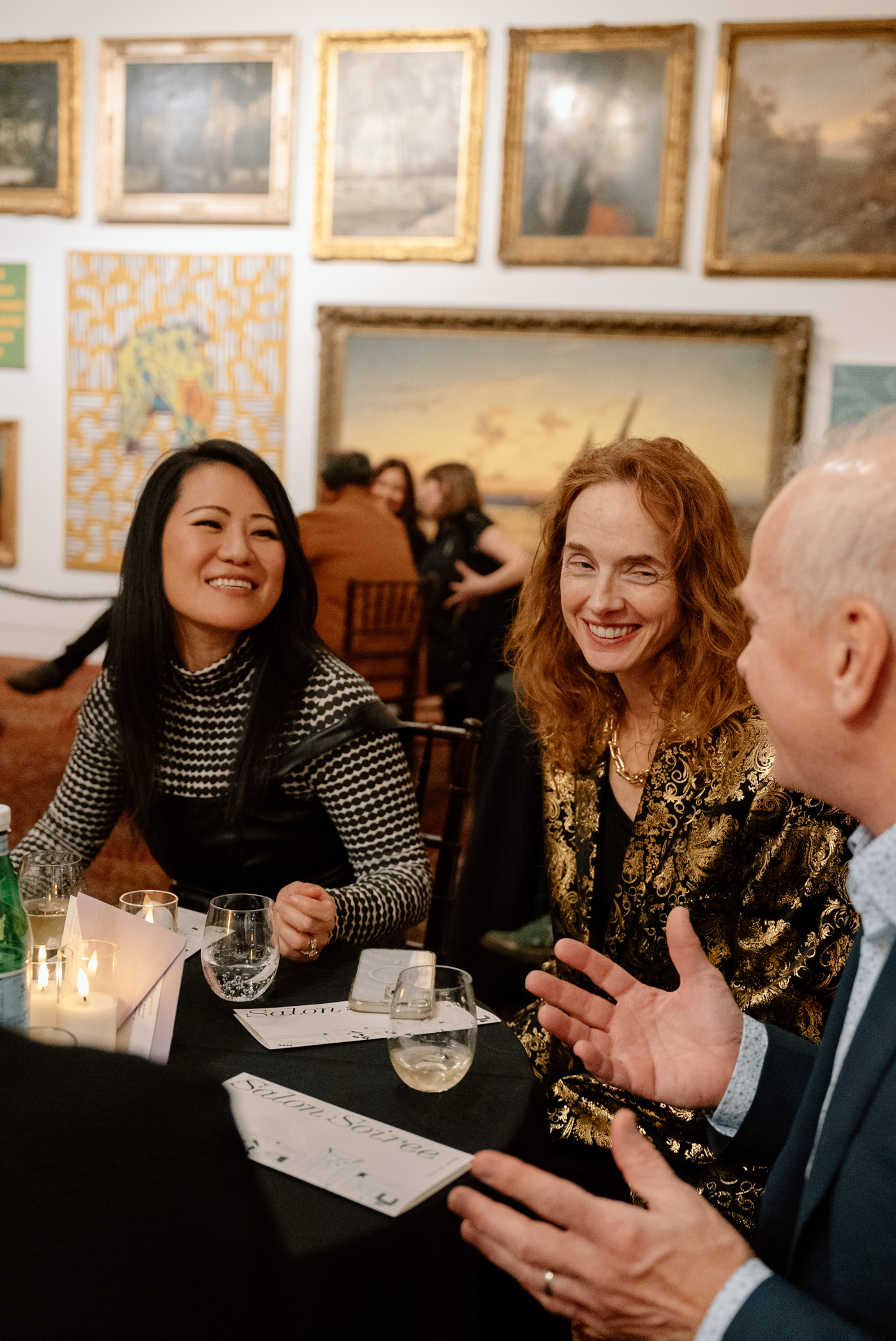 Smiling and chatting people at a table in a large space with paintings on the wall behind them