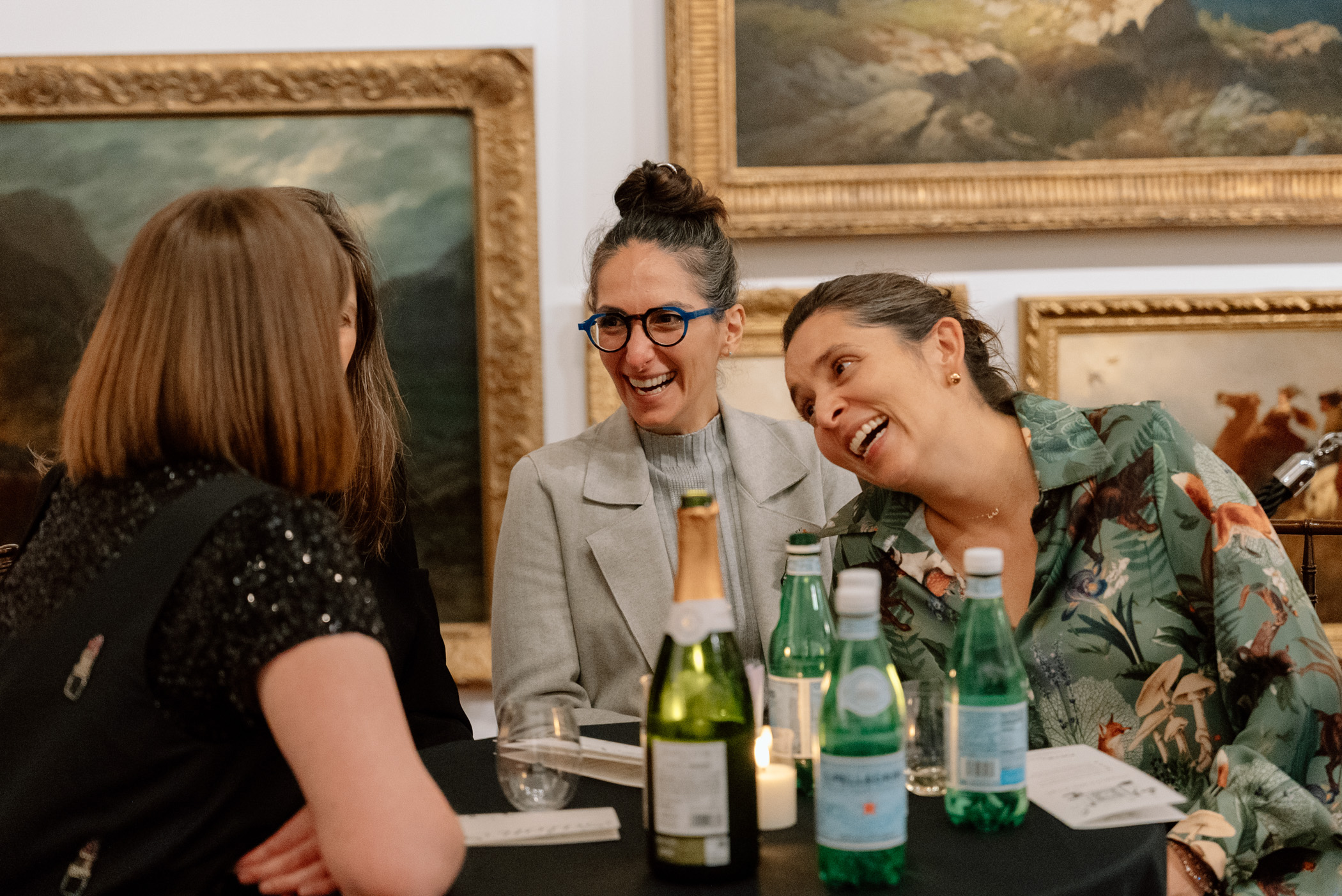 People sitting at a table and chatting in front of a wall covered in paintings