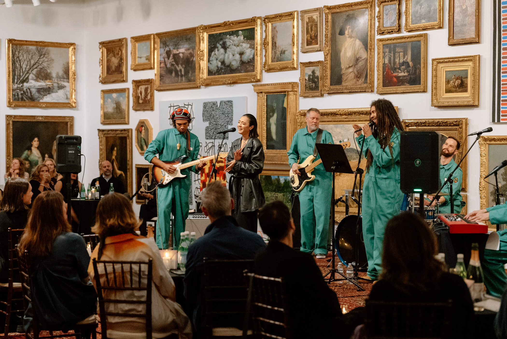 A band performing on an elevated stage in a large room with paintings covering the walls 