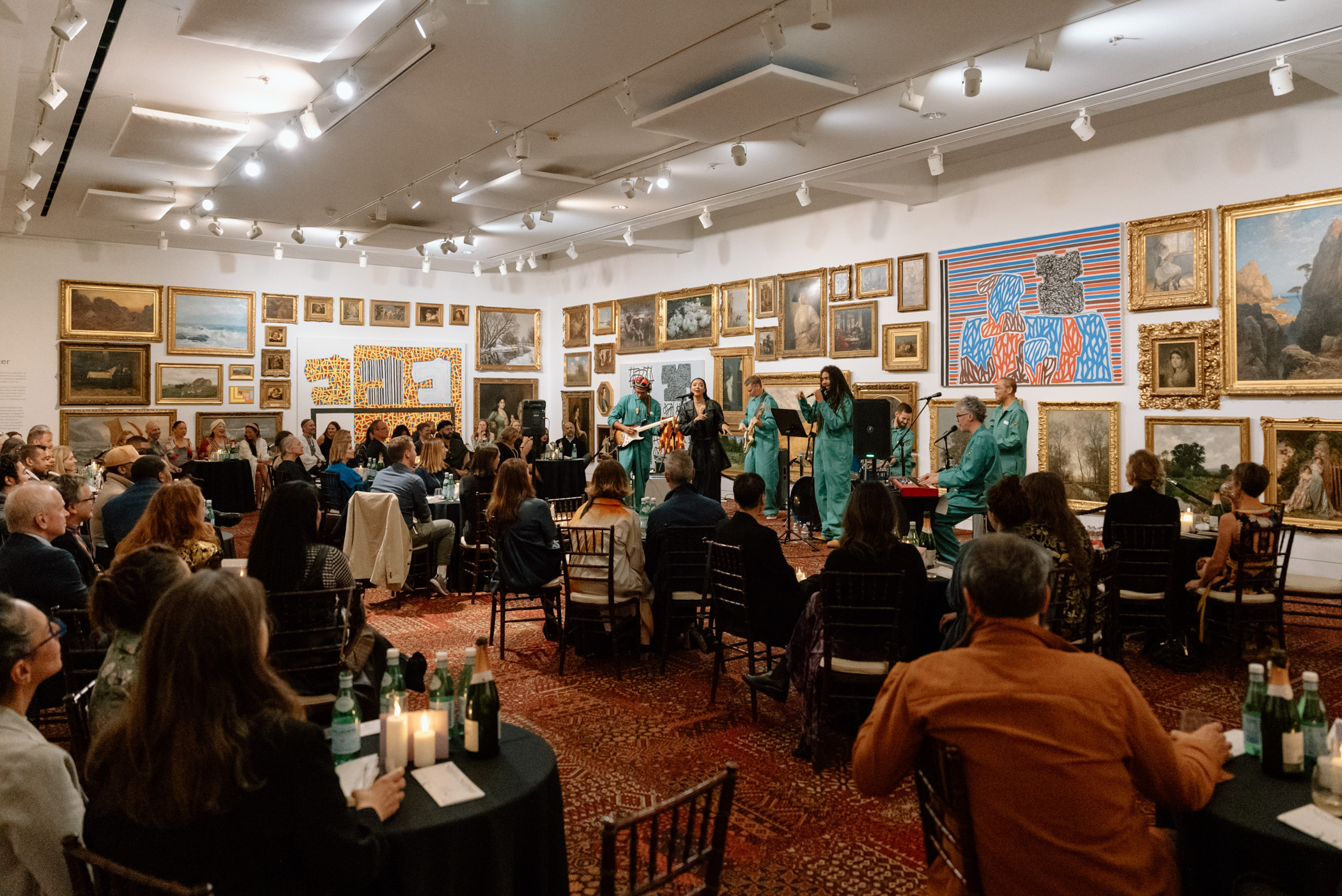 A band performing on an elevated stage in a large room with paintings covering the walls 