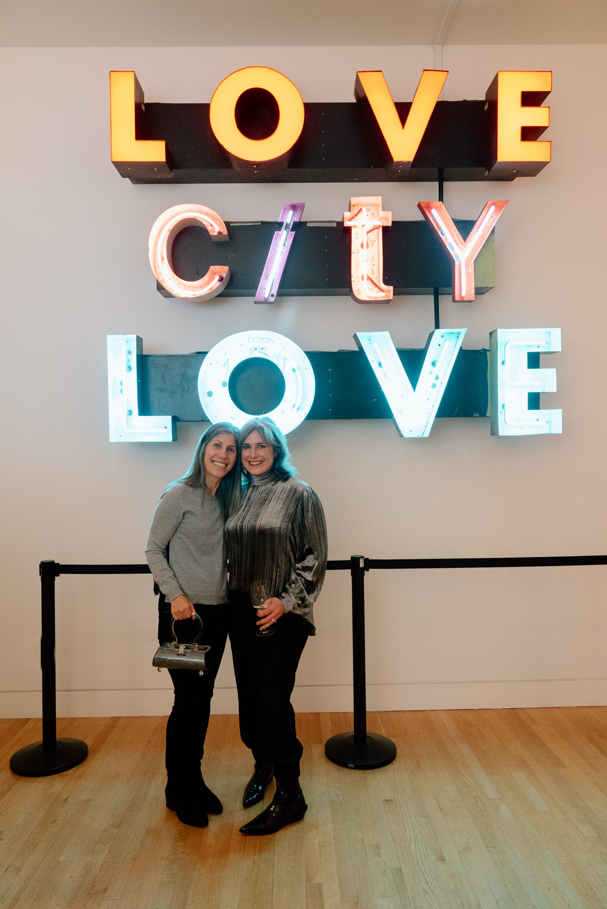Two people smiling and posing for a photograph in front of a neon sign reading Love City Love