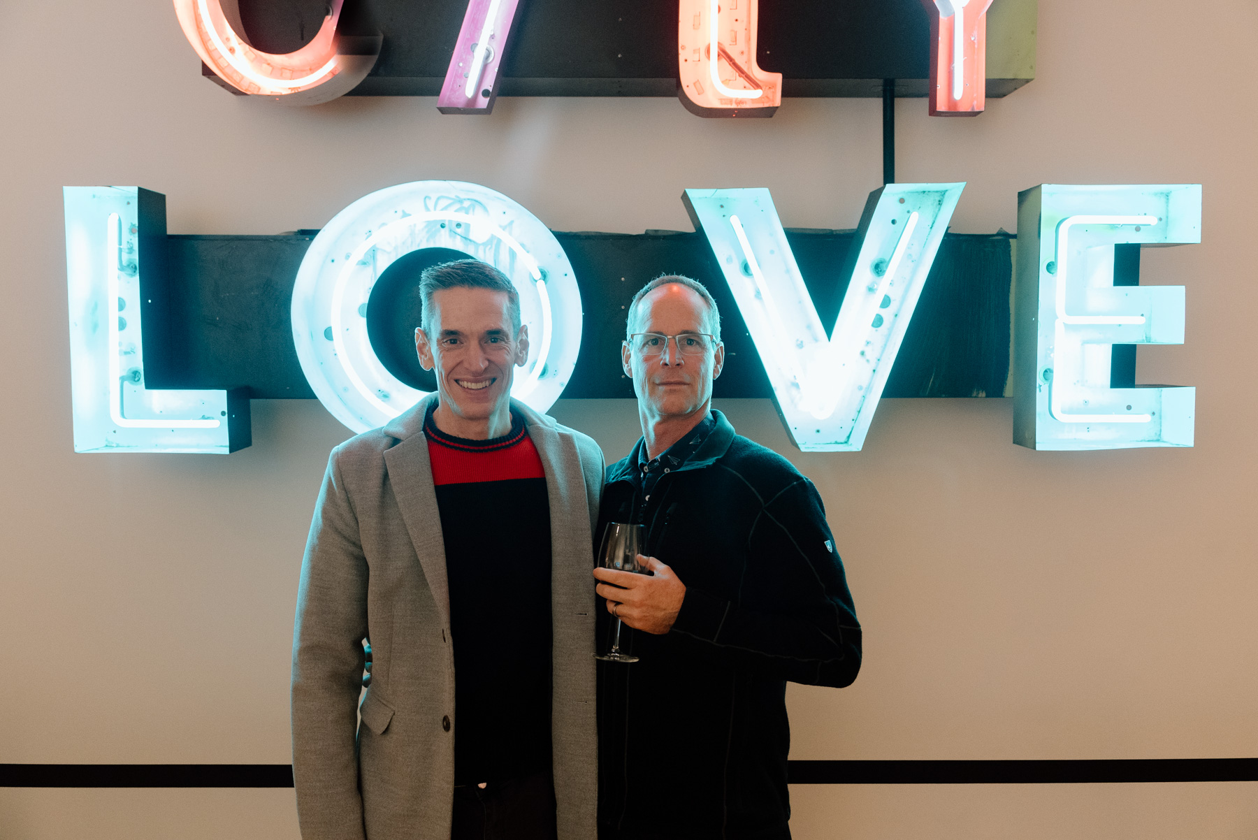 A pair of people smiling and posing in front of a neon sign