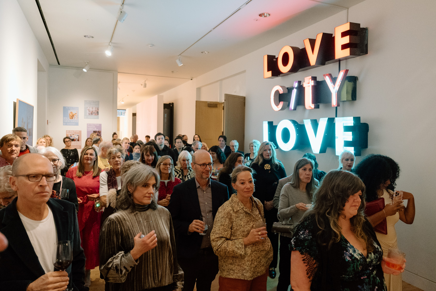 People standing and watching something off camera in front of a sign with the text Love City Love