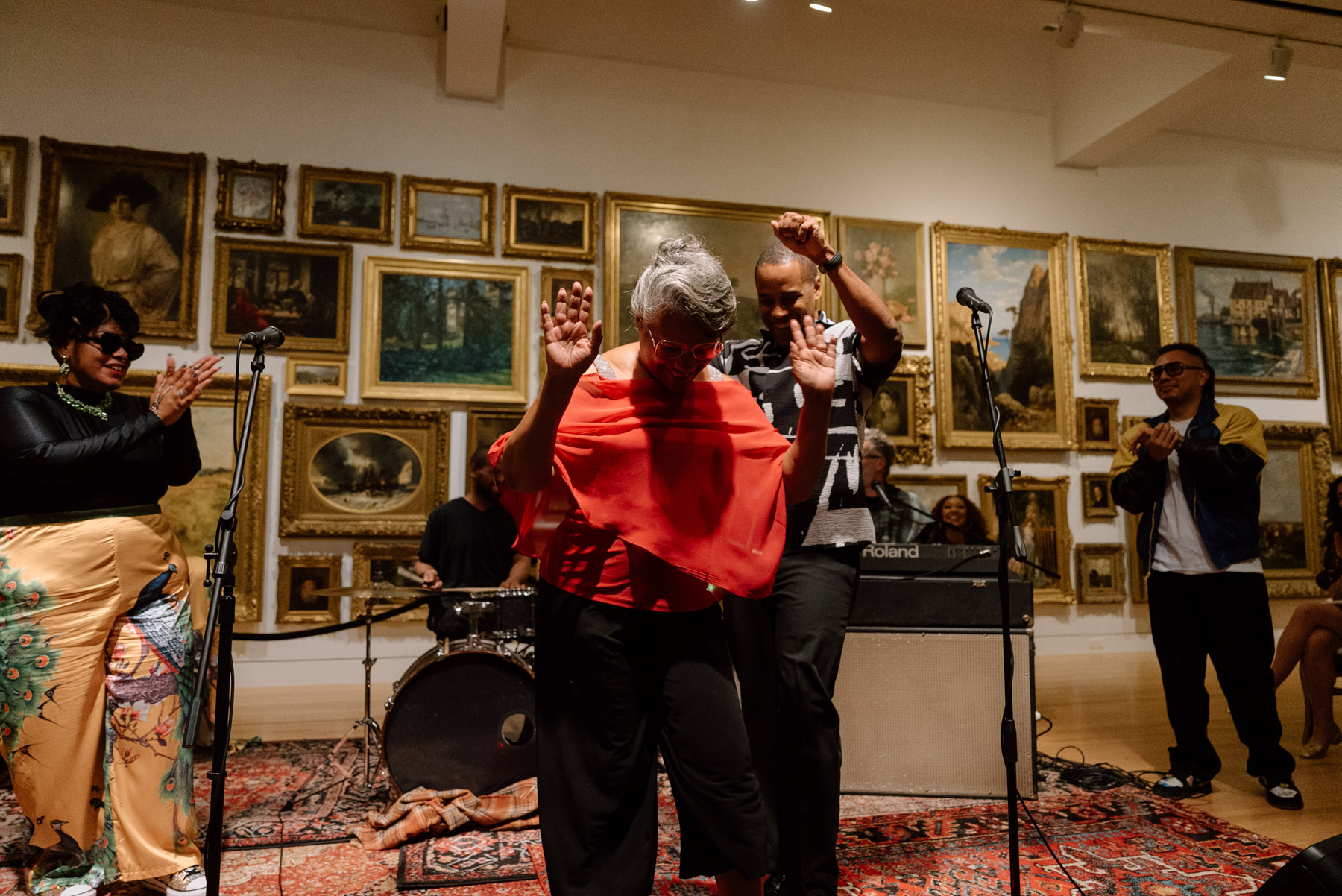 People performing in front of a wall covered in paintings with opulent gold frames