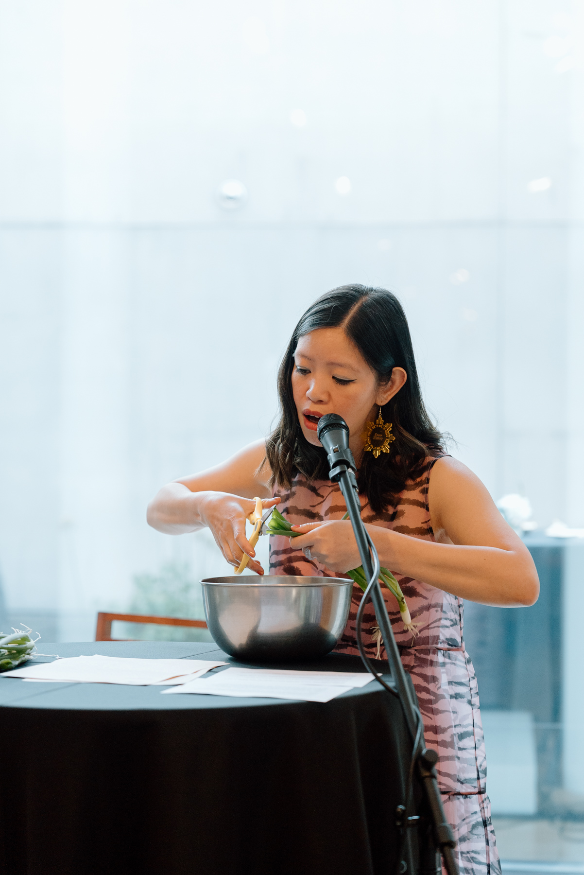 A person reading from a sheet of paper into a mic while cutting green onions with scissors