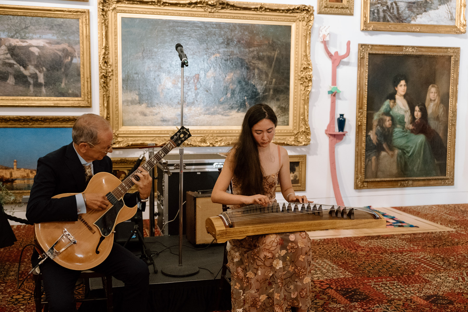 Two people playing musical instruments in front of wall covered on opulent gold paintings