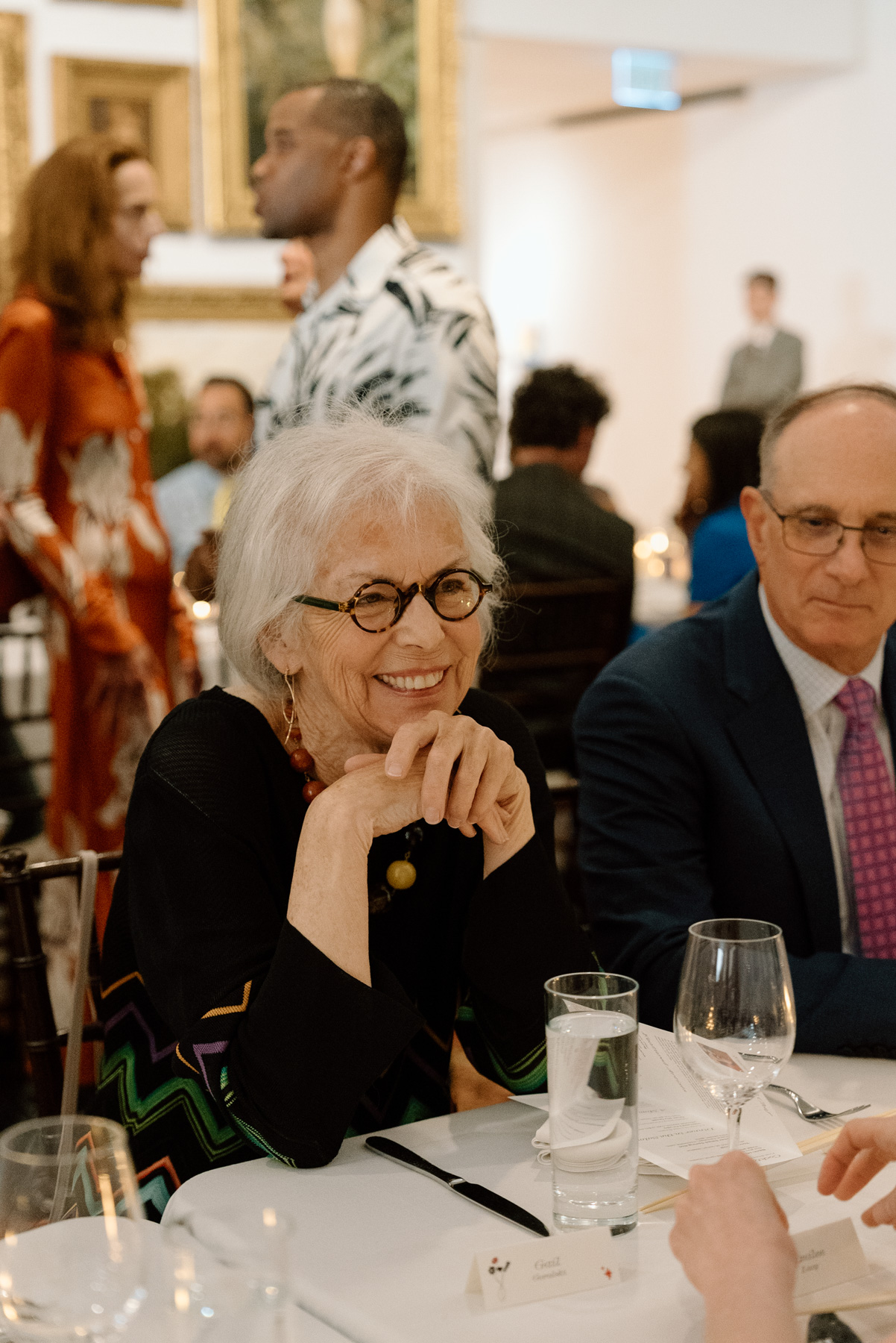 An older woman smiling while sitting at formally laid dinner table