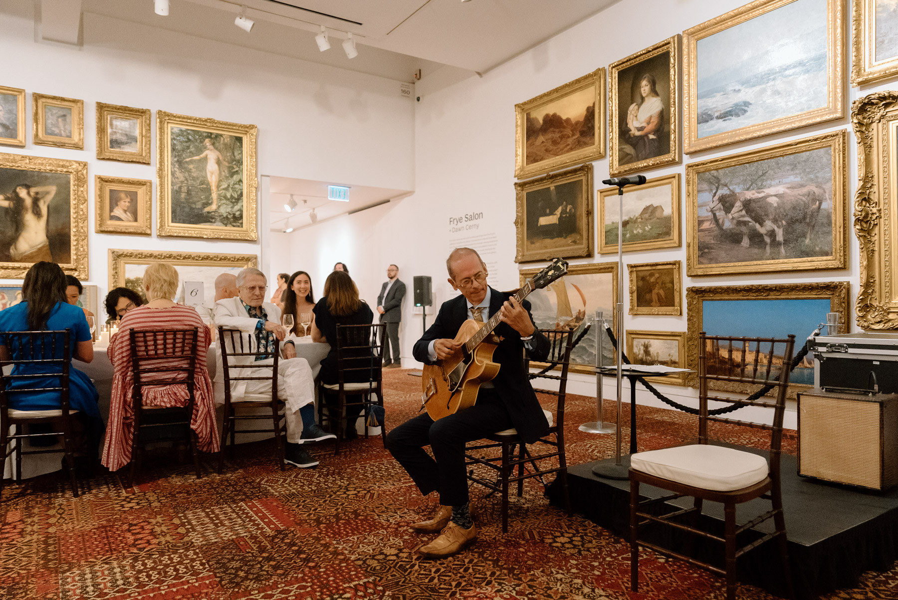 A guitarist performing next to a long dinner table in front of artwork