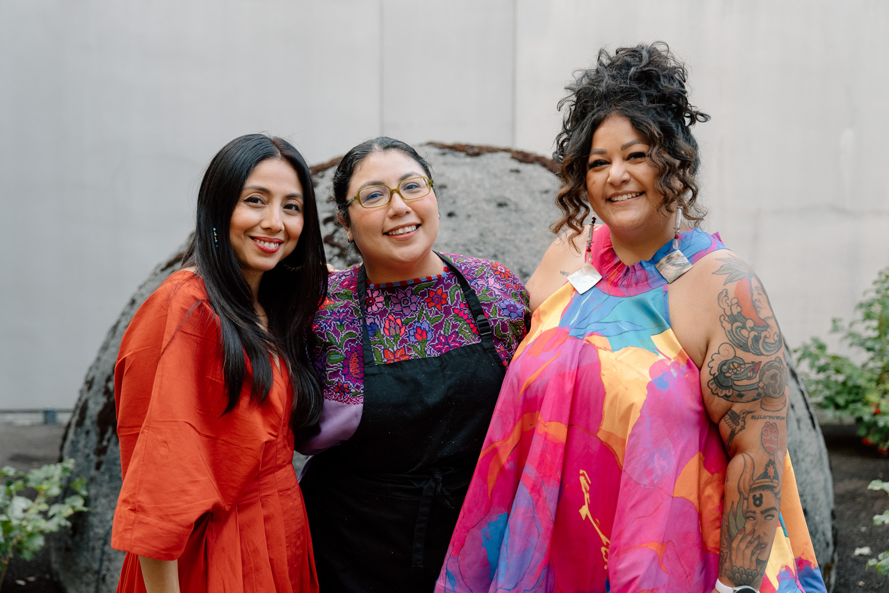Three women in colorful clothing, including one in an apron, in an outdoor courtyard space