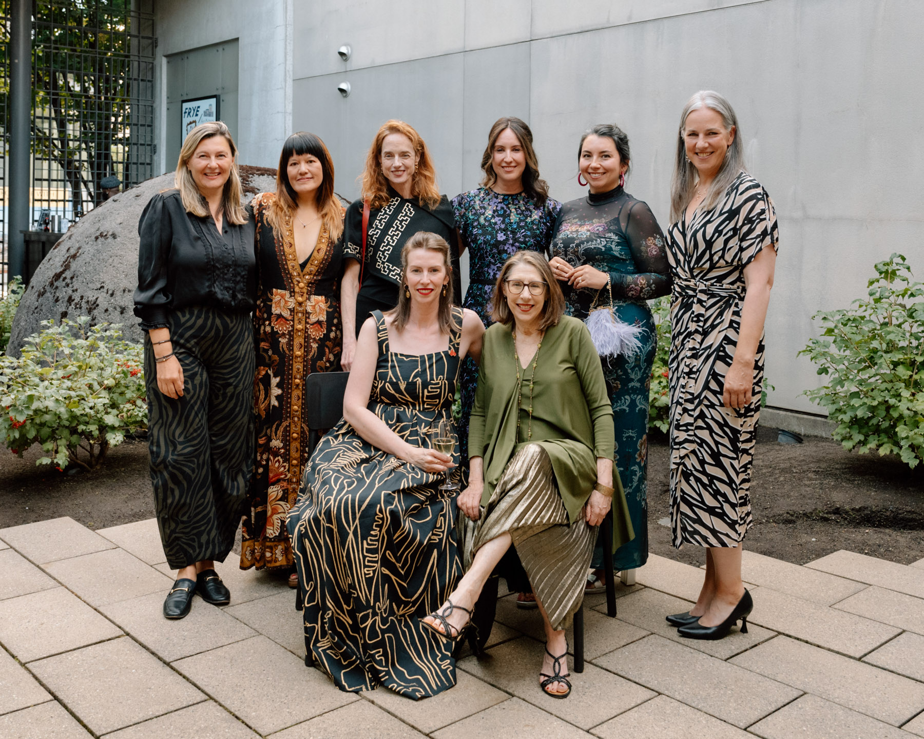 A group of eight women in cocktail party attire posing for a photo in an outdoor courtyard space