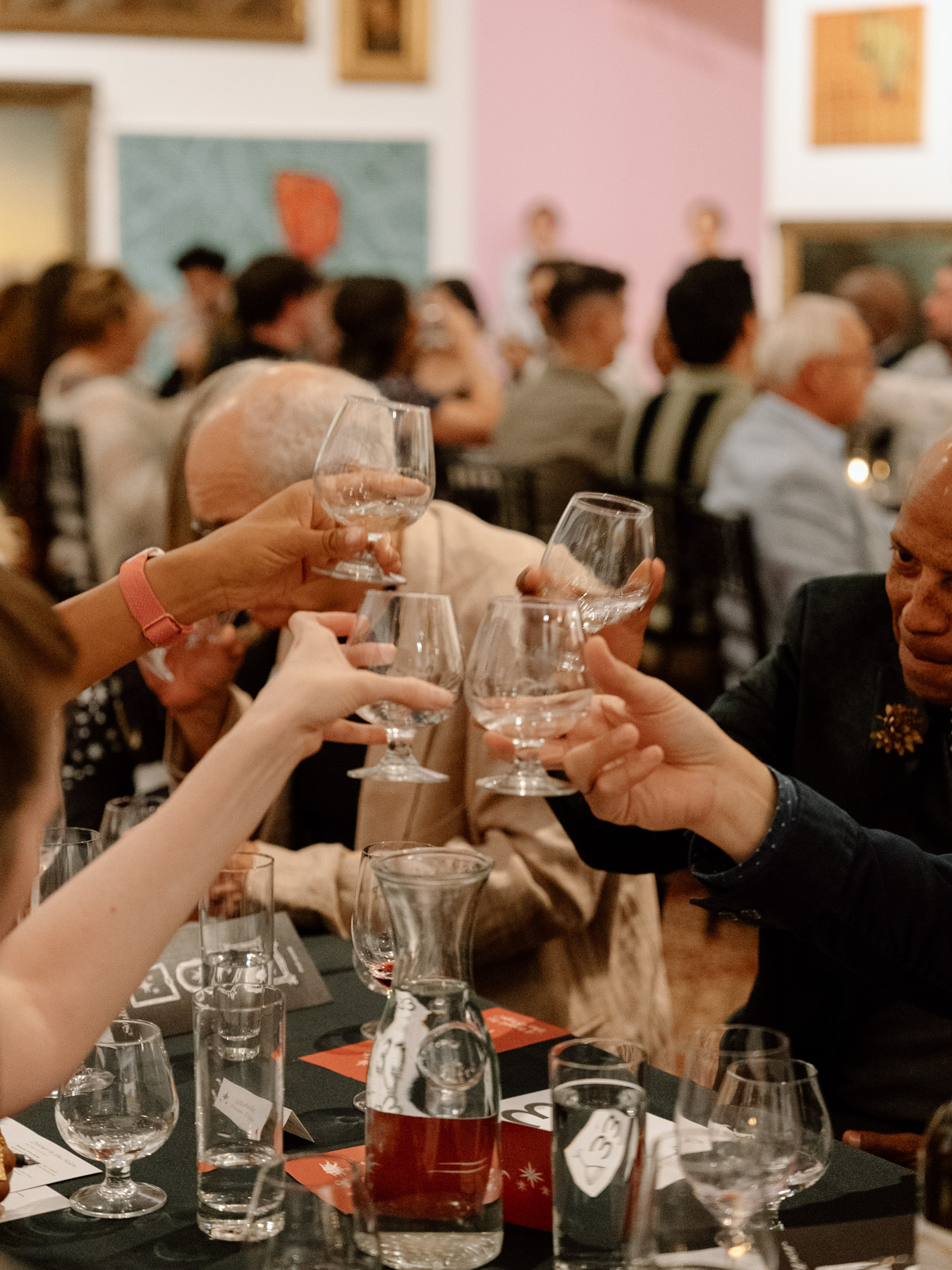 People holding glasses for a toast above a formally laid table in an art gallery space