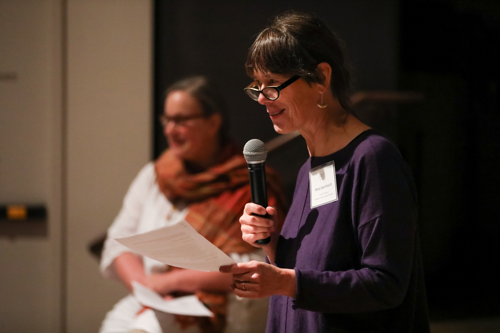 Photo of Mary Jane Knecht speaking into a microphone while presenting at a conference