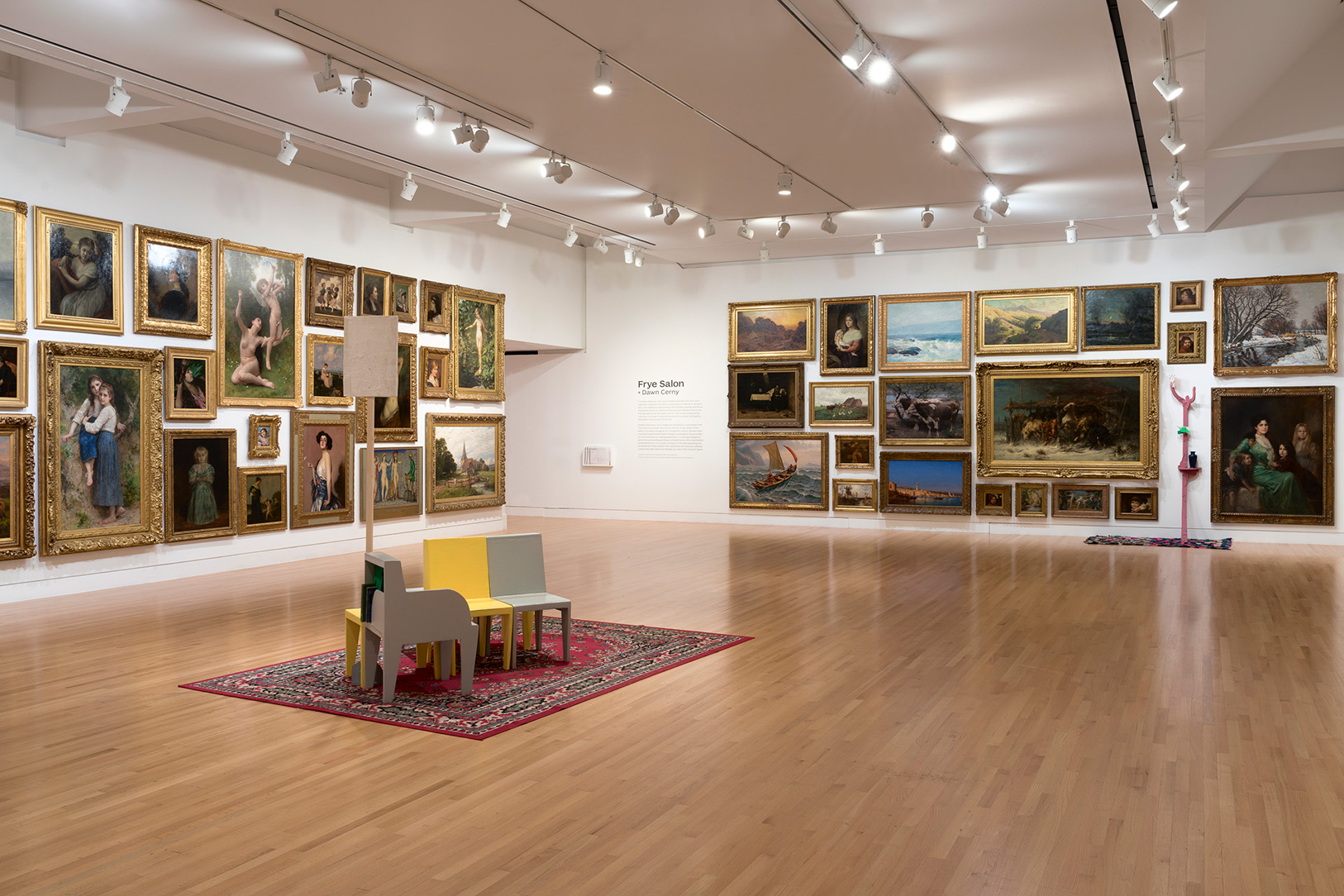 A large room with art covering the walls. Colorful chairs are grouped in the middle of the room.