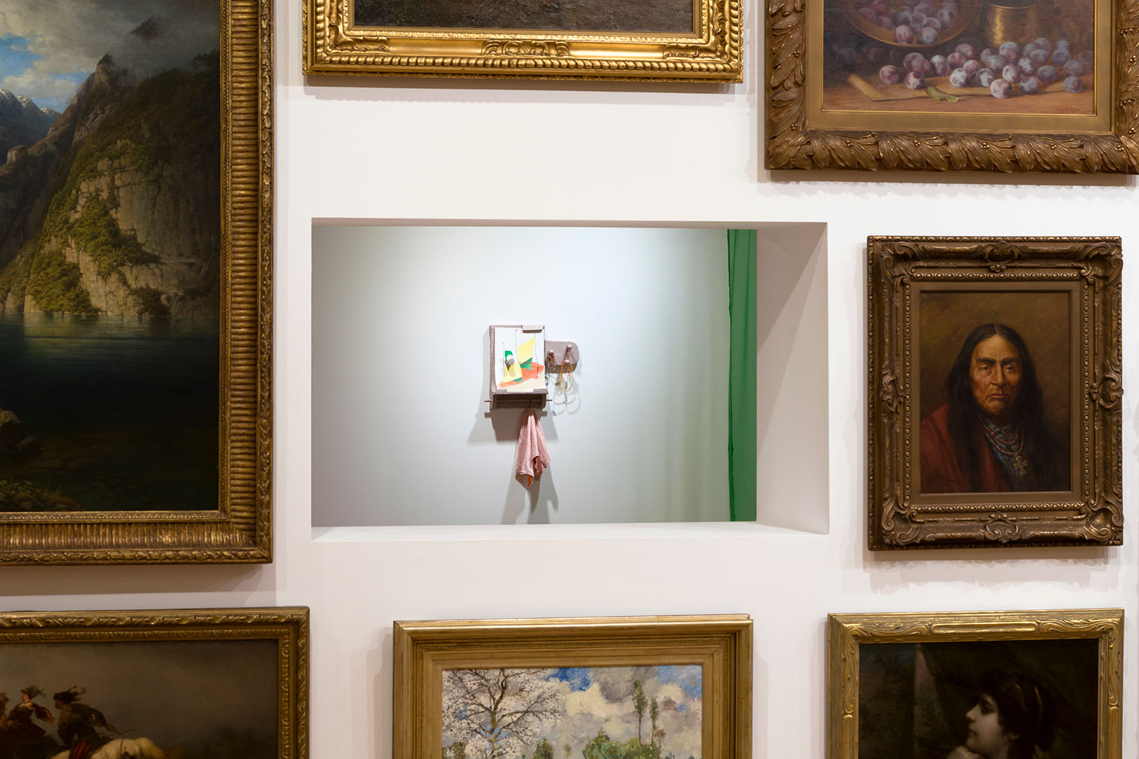 A view through a hole in a wall covered in paintings of a small, wall-mounted artwork on a far wall.