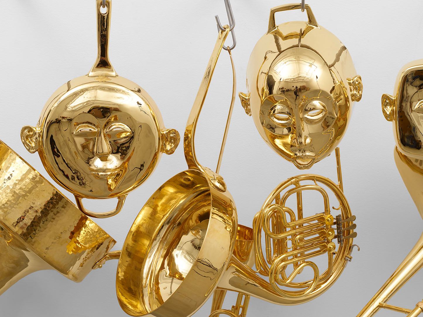 A close up view of artwork in the shape of gold plated pots and pans with faces crafted into them