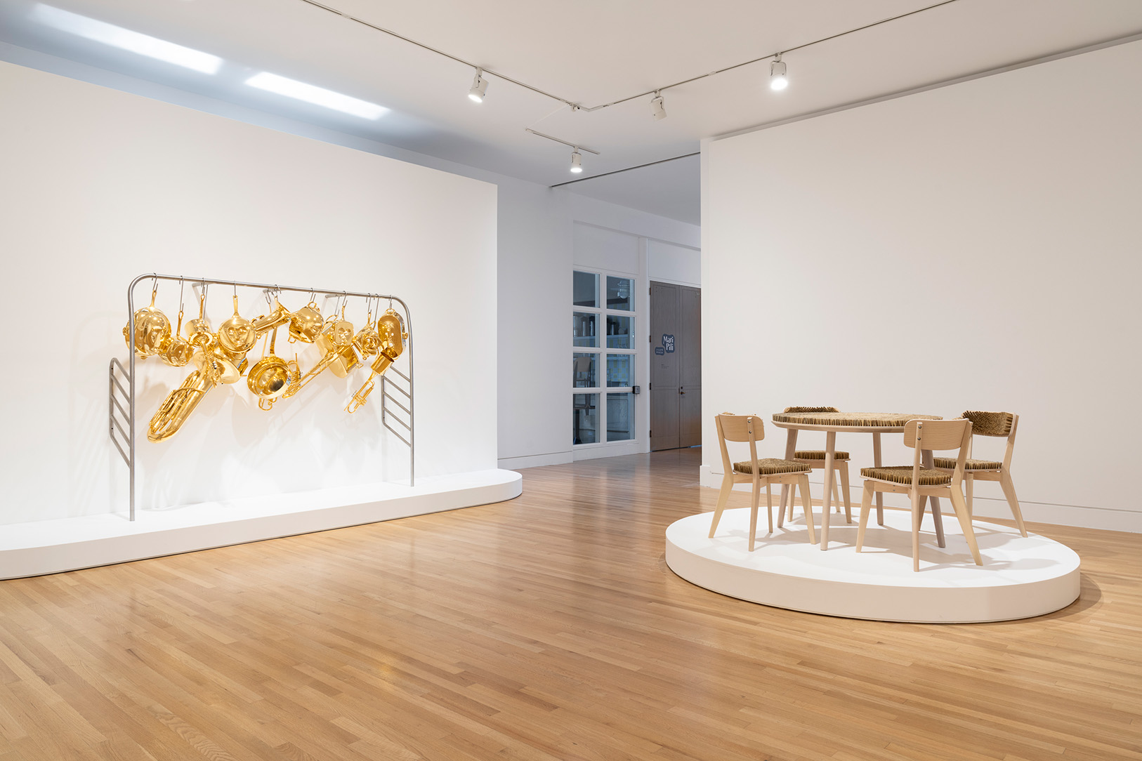 A gallery space with two artworks. On the left are musical instruments and pots fused together and covered in gold, on the right is table covered in bristles