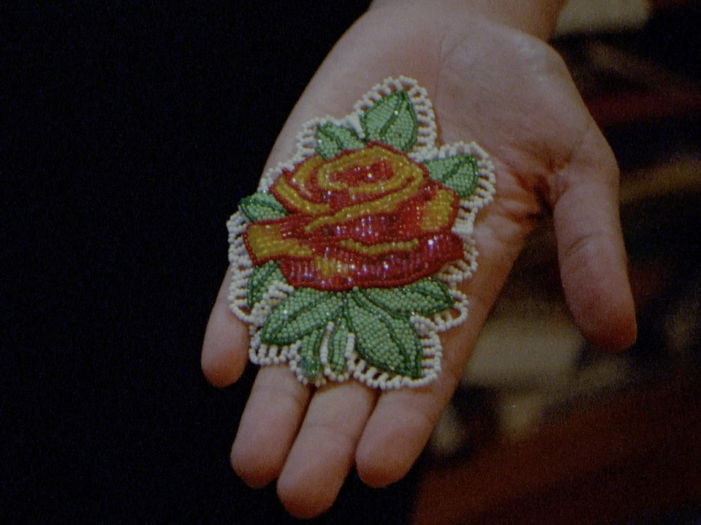A hand holding an embroidered flower from Sky Hopinka's video Kicking the Clouds