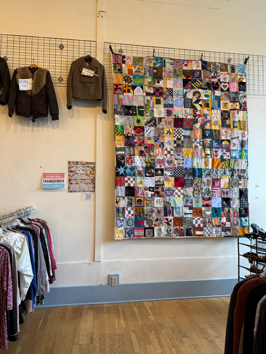 A large colorful quilt hanging on a wall next to a couple of jackets