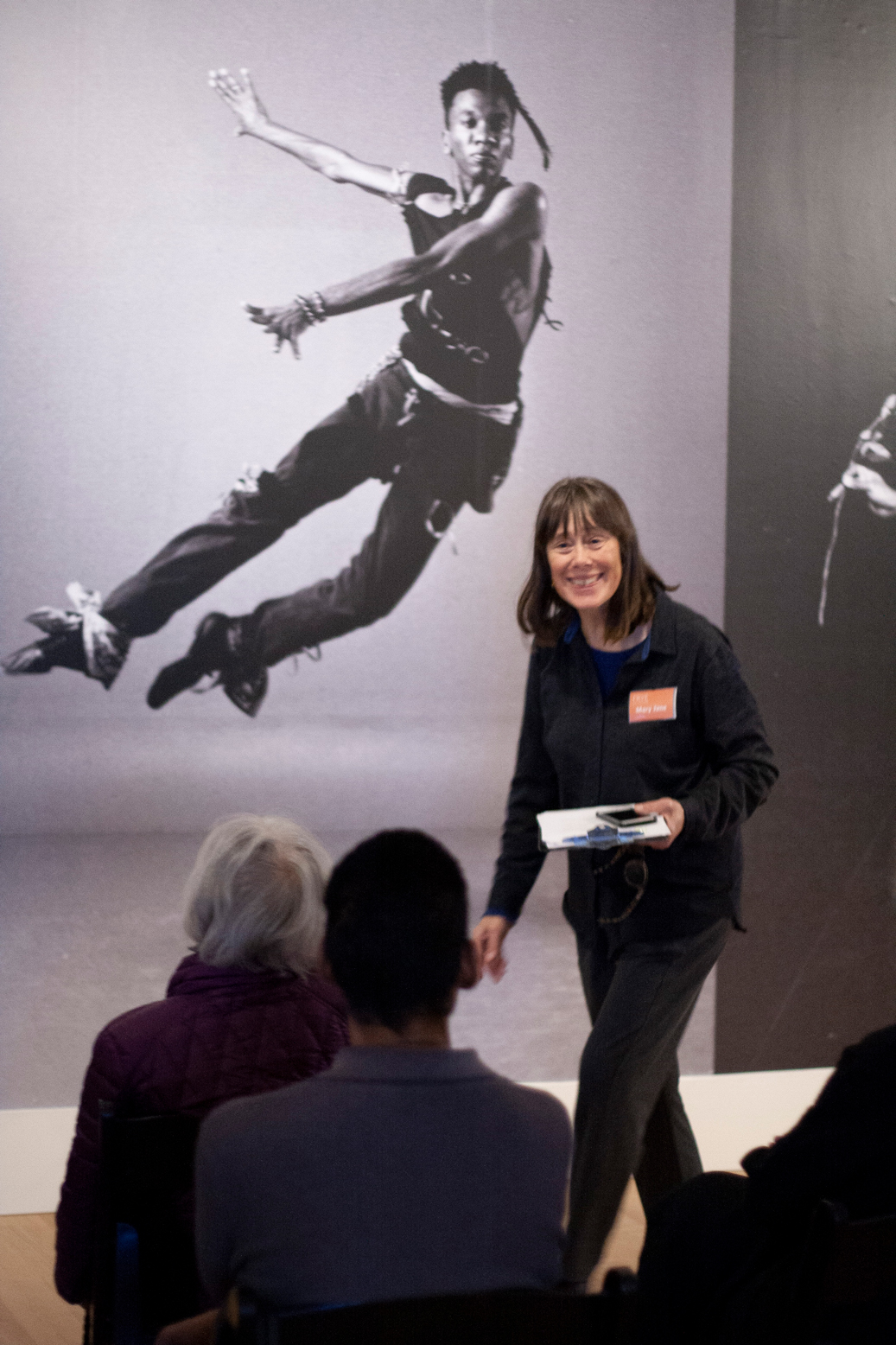 Photo of Mary Jane Knecht leading an artwork discussion in front of a large image of a dancer in a Frye gallery