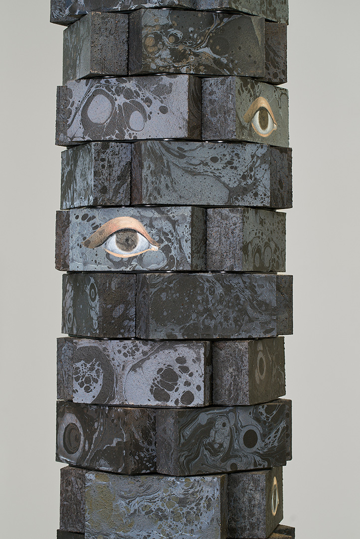 A detail view of stacked bricks with painted eyes and designs in oil and acrylic