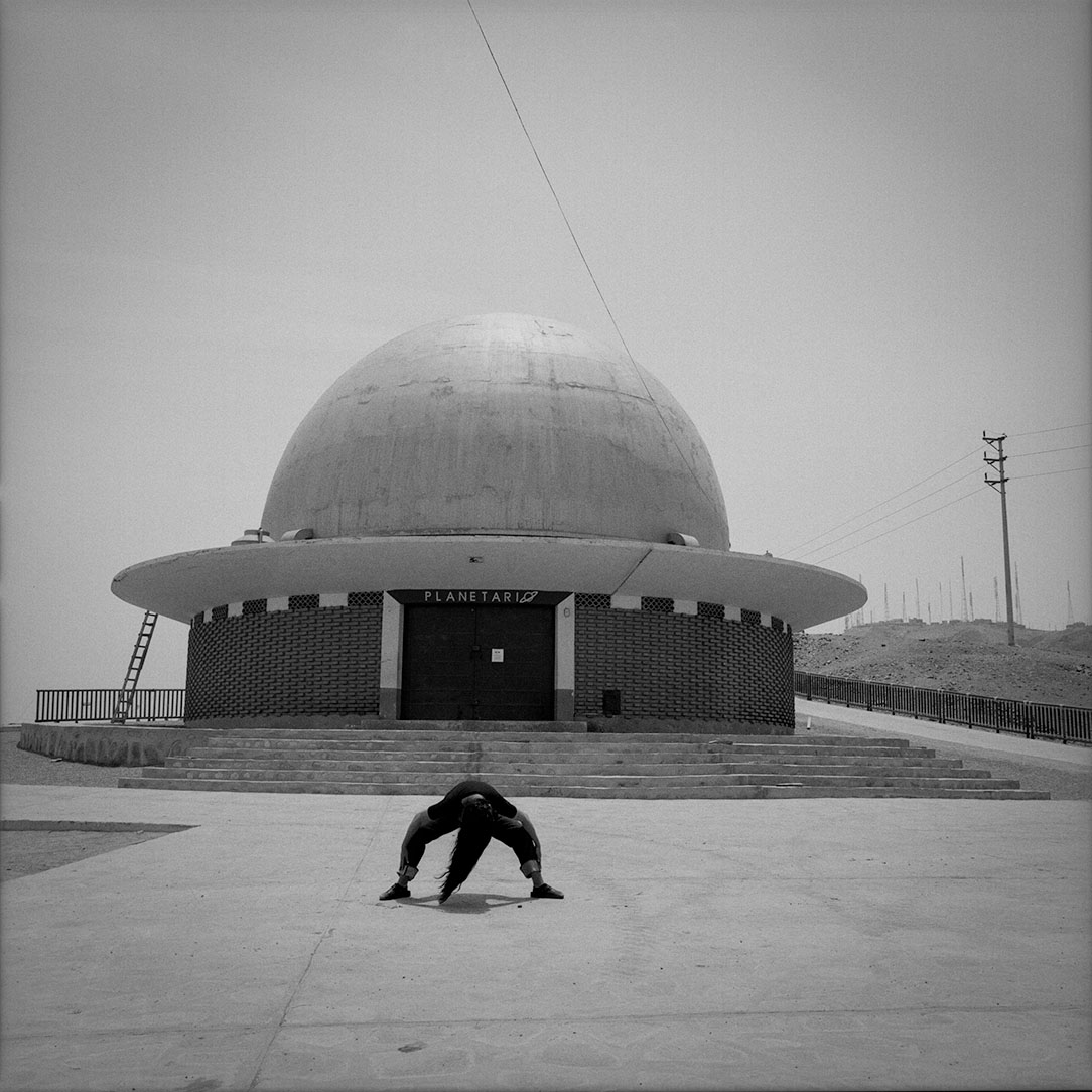 A black and white film photograph of a woman posing in front of a planetarium