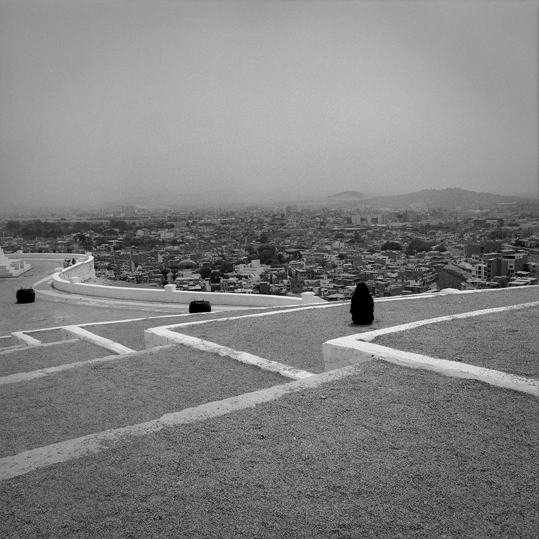 A black and white film photograph of a woman sitting on large terraced steps above a city