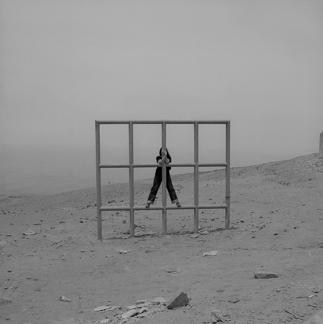 A black and white film photograph of a woman posing with a geometric wooden structure