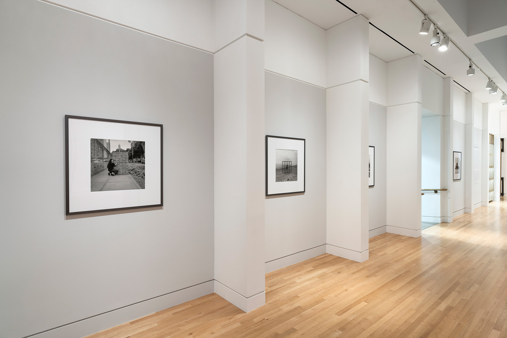 A series of black and white photographs mounted in frames on a long wall in a museum gallery space