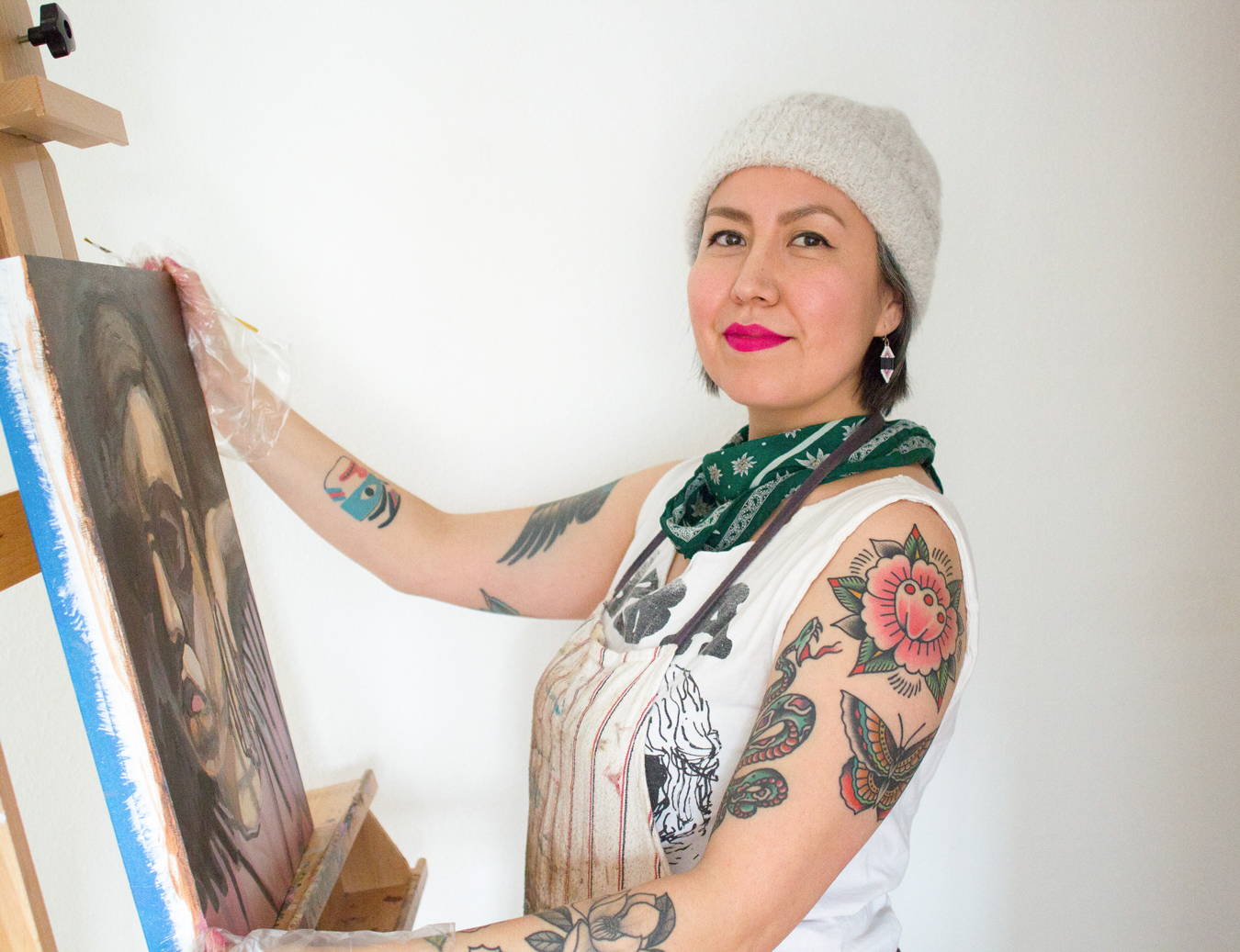 Photo of artist Naomi Parker standing at an easel that has a painted canvas sitting on it; she holds the canvas and a paintbrush in her hands