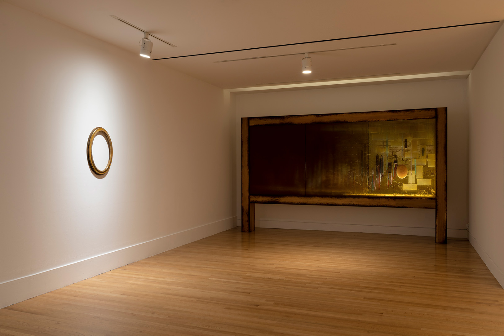 An empty oval picture frame on a wall near a large artwork installation with ribbons and other items disguised behind a semi-transparent screen