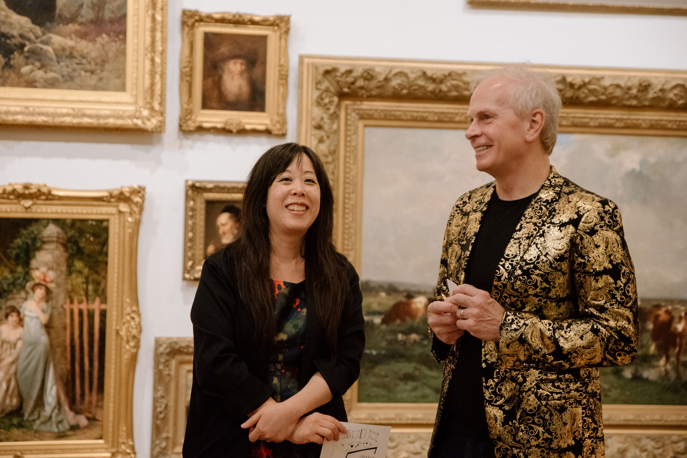 Two people chatting and smiling in front of a wall covered in art