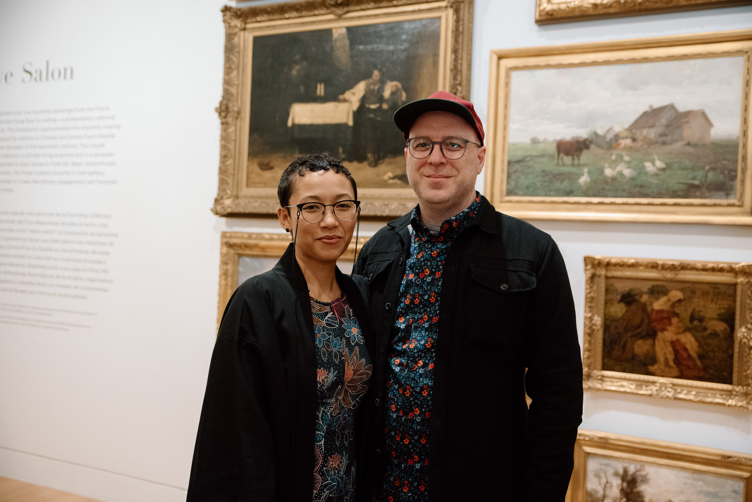 Two people smiling and standing in front of a wall covered in art