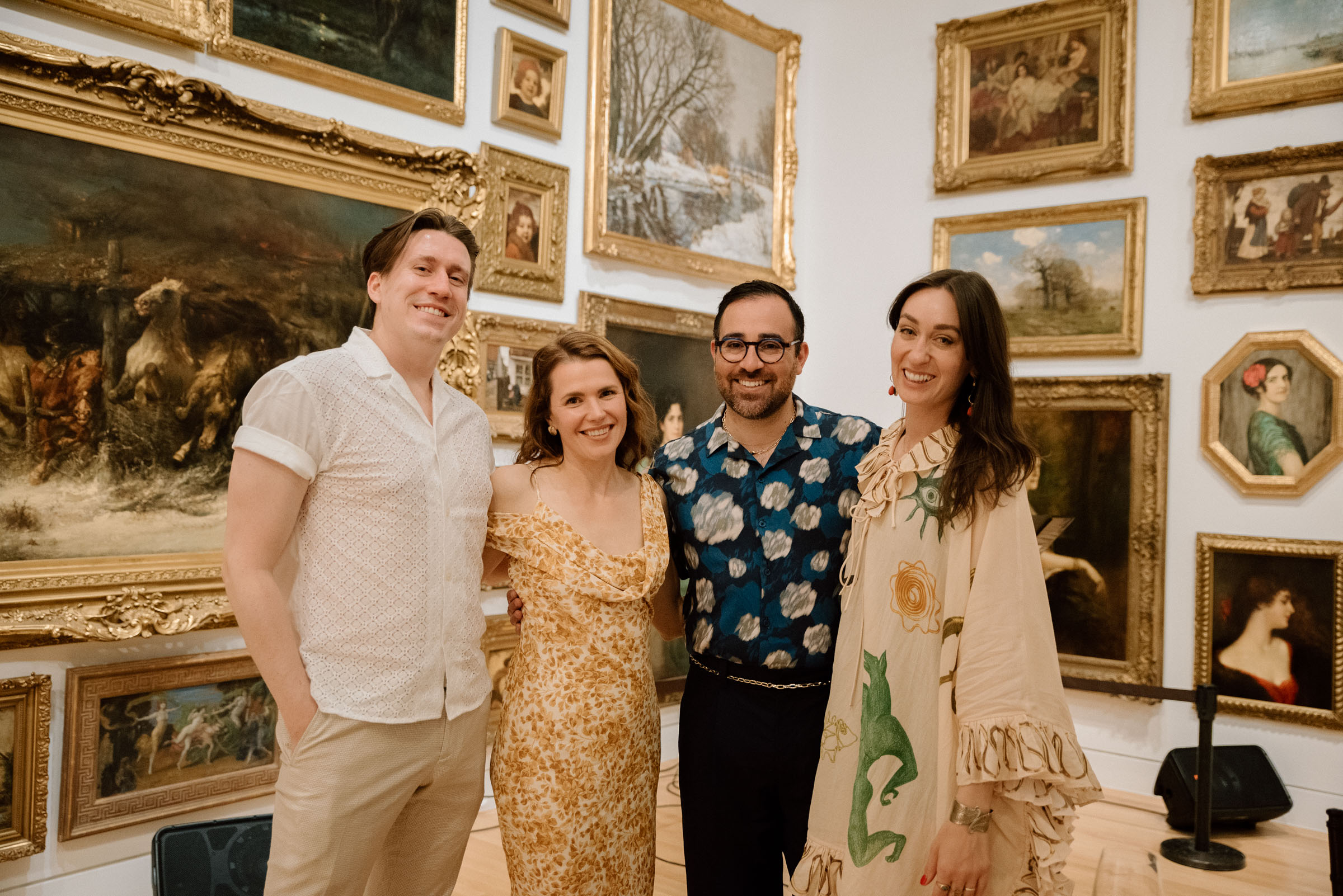 People standing and smiling in a group in front of a wall covered in paintings