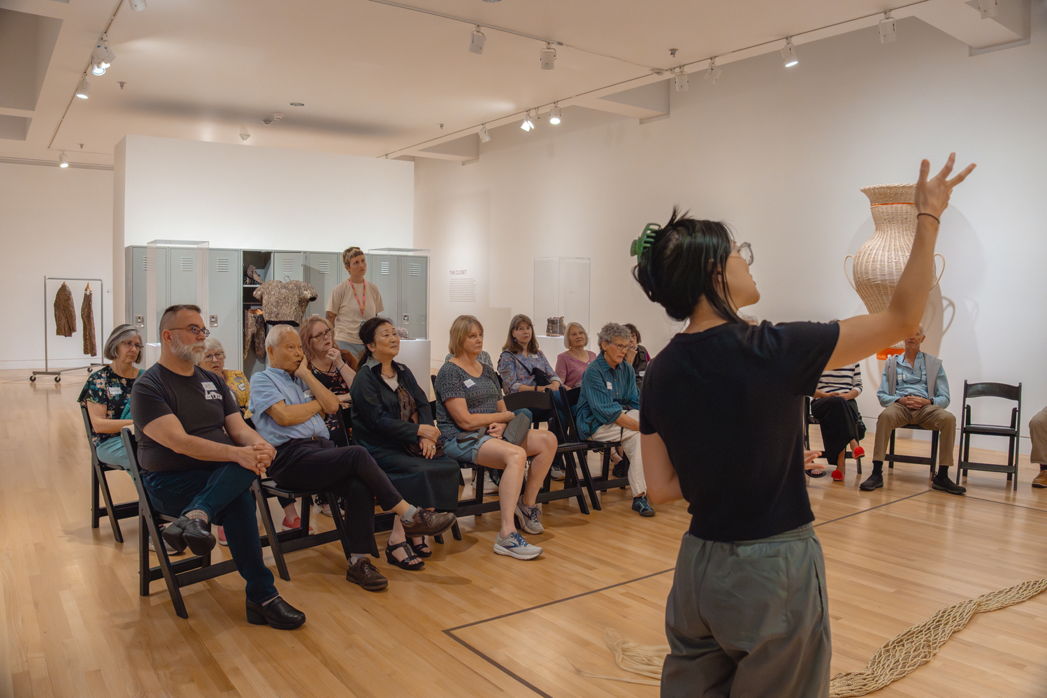 Teaching artist gesturing in front of a group of older adults seated in a gallery