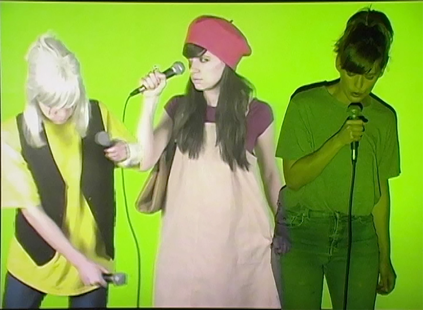 A still from a video of a person playing three members of a band in front of a green screen