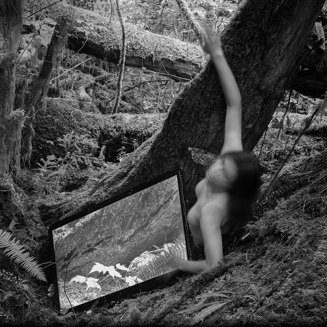 A black and white image of a nude human figure in a natural, forested landscape with their body partially obscured by movement and a large LCD screen