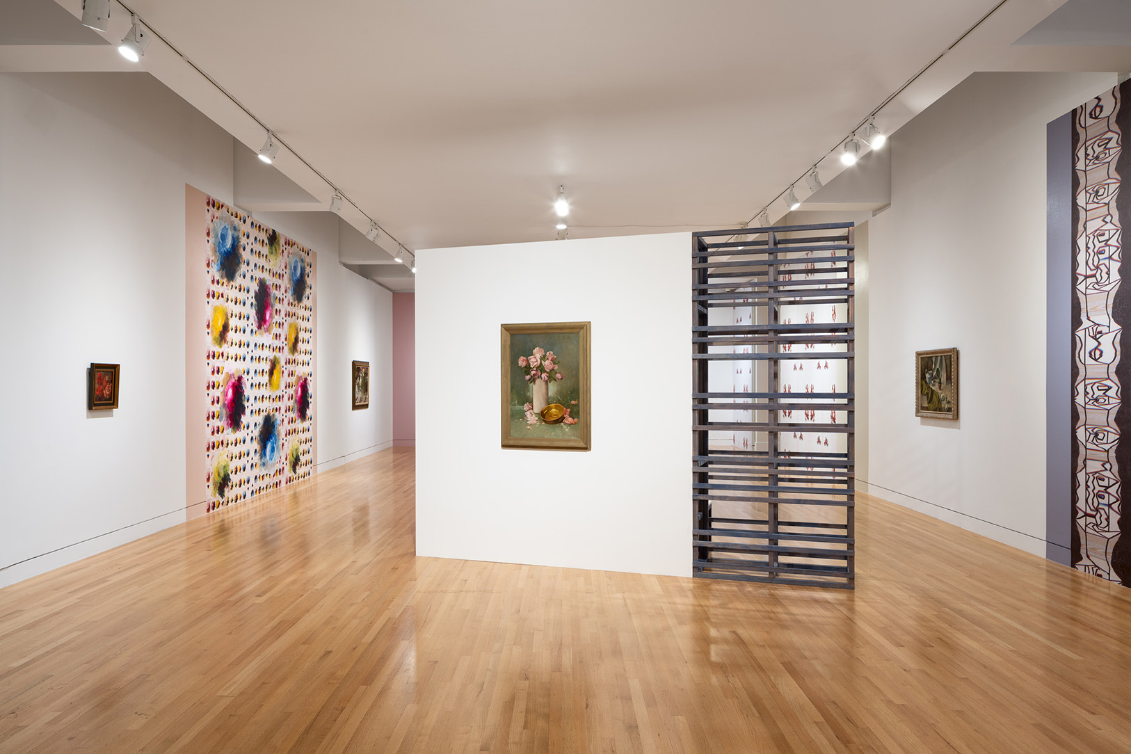 A large gallery space hung with a few still life paintings of flowers and large wall sections covered in colorful wallpapers