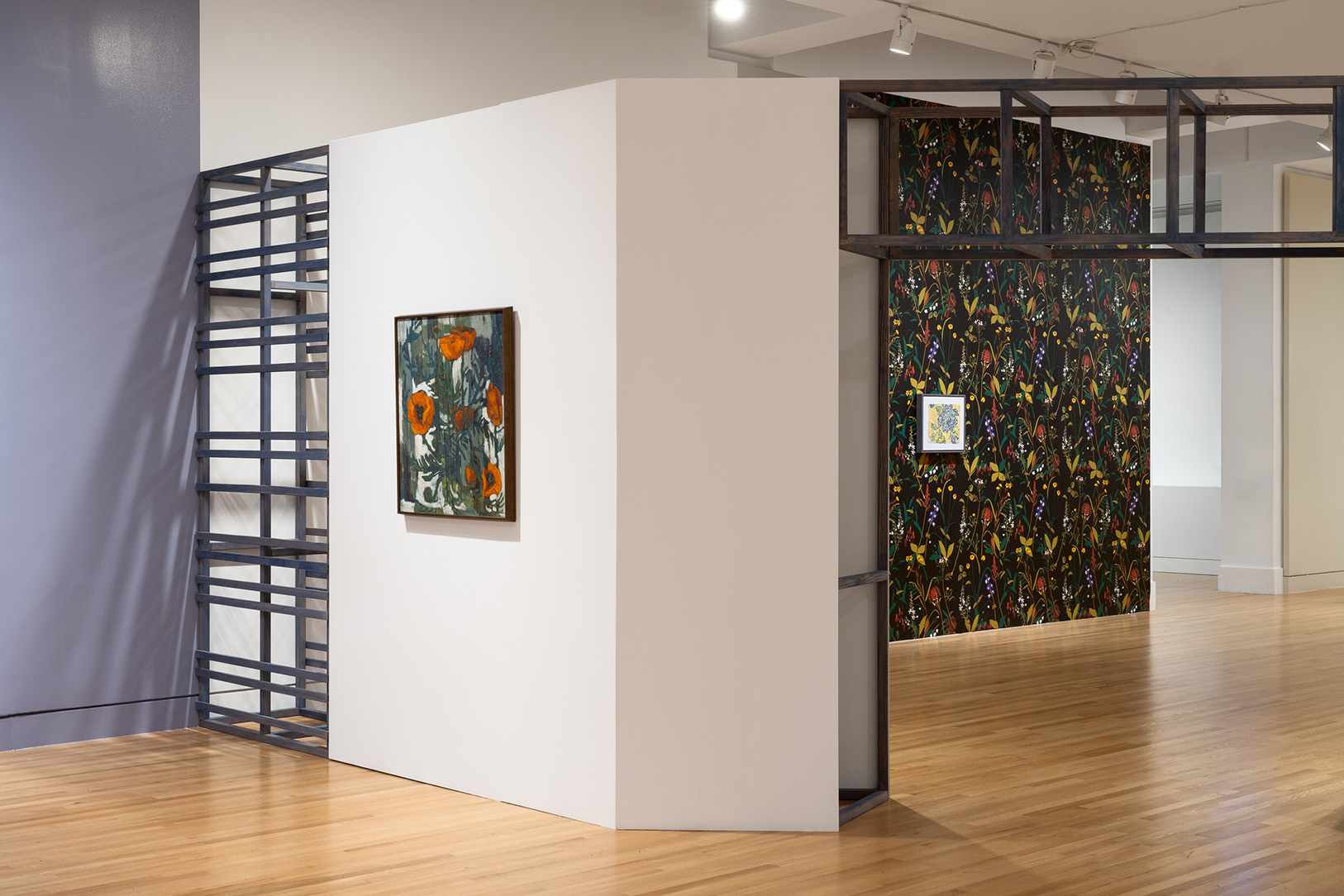A large gallery space hung with a few still life paintings of flowers and large wall sections covered in colorful wallpapers