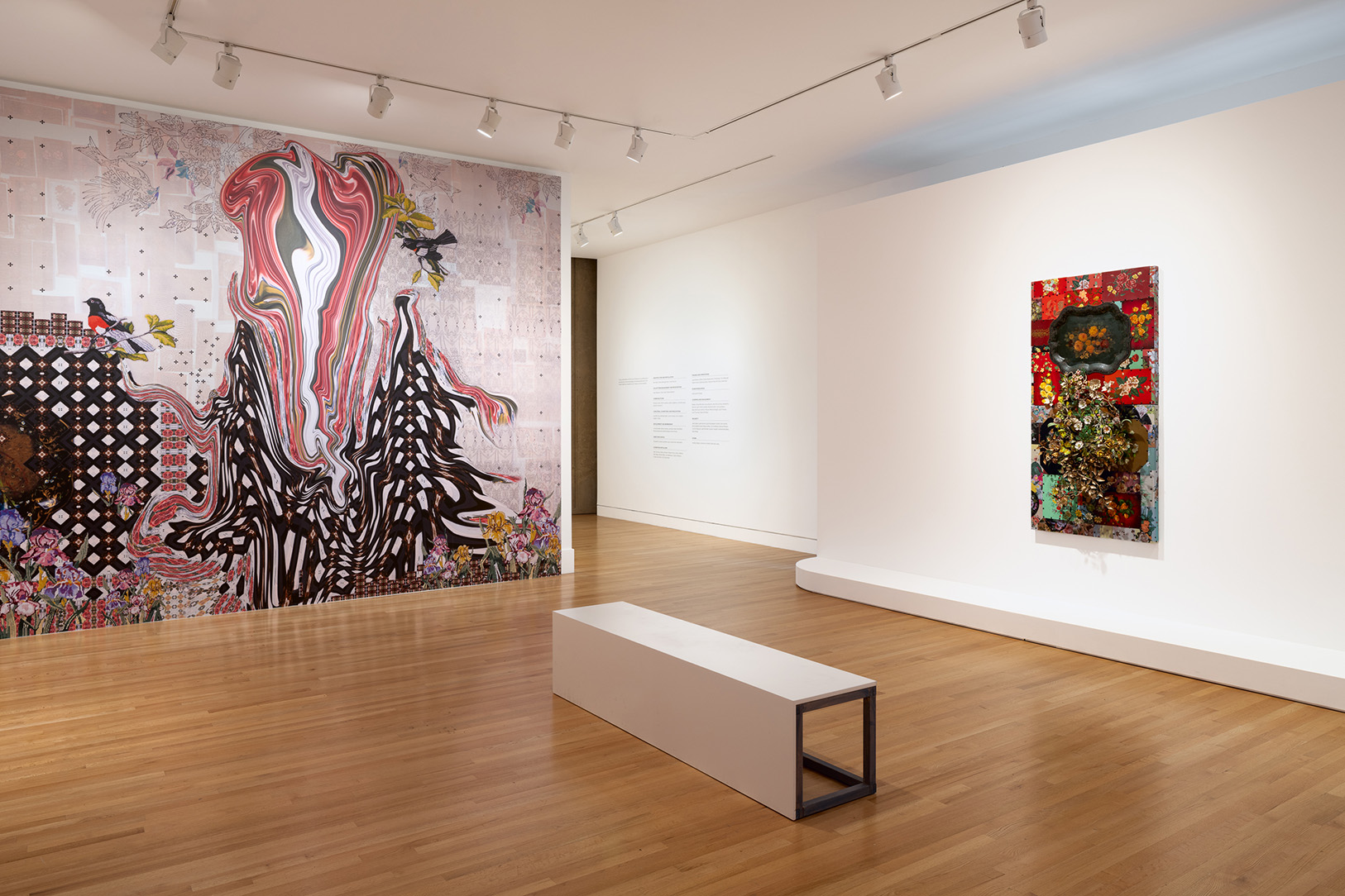 A large gallery space hung with a few still life paintings of flowers and large wall sections covered in colorful wallpapers