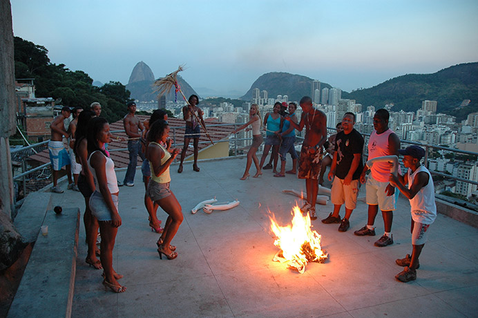 Still from a video of people dancing around a small fire on top of a building