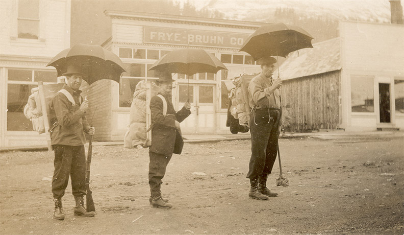 People in hiking gear holding umbrellas in Alaska in the early 20th century